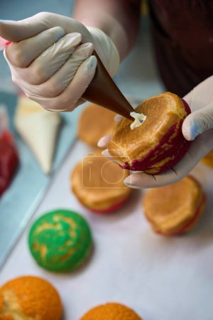 Pastelero de primer plano exprimiendo la crema batida de la bolsa de pastelería en hueco en choux au craquelin pastelería, relleno profiteroles, eclairs o chouquettes con relleno