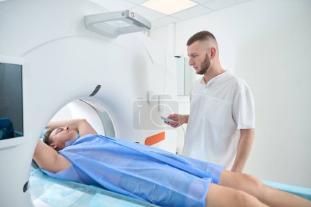 Männchen mit erhobenen Armen über dem Kopf liegend, während Röntgenbild CT-Tisch mit manueller Steuerung in Portalöffnung bewegt