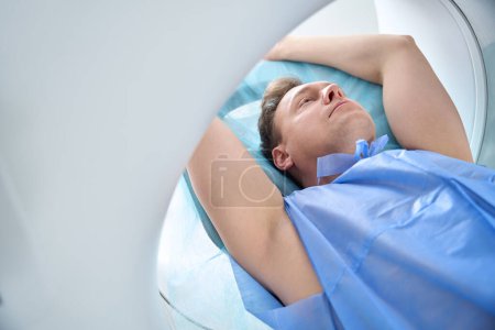Ausgeschnittenes Foto des Patienten mit erhobenen Armen über dem Kopf liegend in der CT-Portalöffnung
