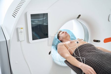 Foto de Persona adulta masculina con electrodos ECG colocados en el pecho acostado en posición supina dentro de la abertura del pórtico CT - Imagen libre de derechos