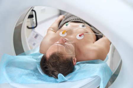 Mann mit an Brust befestigten EKG-Elektroden liegend in CT-Portalöffnung