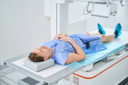 Paciente adulto acostado en posición supina sobre mesa radiográfica con piernas paralelas al receptor de imagen