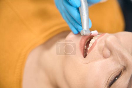 Close-up skilled dental therapist equipped with specialized tools meticulously cleaning female client teeth, aiming for a pristine finish, aesthetic medicine clinic