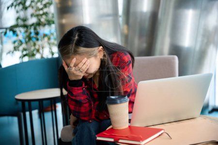 Photo for Young tired female IT employee with headache touching her head during work at table in coworking office. Concept of modern freelance or remote work - Royalty Free Image