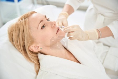 Foto de Cliente femenino que asiste al procedimiento de inyección de contorno, corrigiendo la forma de sus labios con la ayuda de relleno de ácido hialurónico, primer plano - Imagen libre de derechos