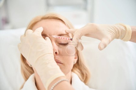 Photo for Close-up cosmetician filling client nasolabial folds with the fillers based on hyaluronic acid to lift skin well and to smooth out wrinkles, rejuvenating and moisturizing - Royalty Free Image