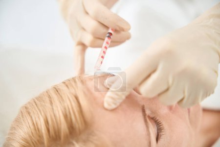 Photo for Close-up doctor making microinjections of filler with little syringe to female client forehead, face oval modelling, wrinkles smoothing, aesthetic medicine - Royalty Free Image