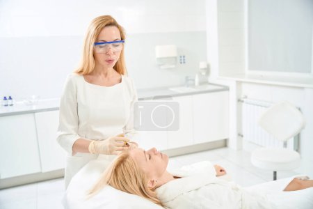 Attentive dermatologist making microinjections of plasma into female client scalp, hair plasmolifting, fight with seborrhea and itchy scalp, aesthetic medicine clinic