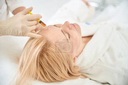 Photo for Close-up cosmetologist introduction into the female client skin her own platelet-enriched plasma, making injections in forehead to remove wrinkles and age-related skin changes - Royalty Free Image