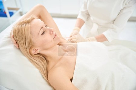 Concentrated blond woman attending cosmetologist office to take the injections of botulinum toxin to cope with the delicate problem of excessive sweating, hyperhidrosis treatment