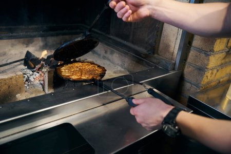 Partial male chef frying pancake in pancake maker in burning fire place in restaurant. Concept of delicious healthy eating
