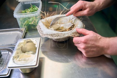 Foto de Chef masculino parcial poniendo crema en ostra en plato de nido en la mesa en el restaurante. Concepto de deliciosa alimentación saludable - Imagen libre de derechos