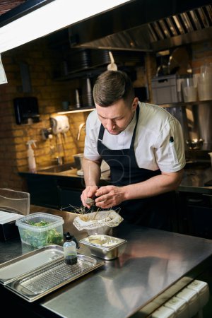 Téléchargez les photos : Chef caucasien saupoudrer d'épices avec une passoire à thé dans une huître dans un nid à table au restaurant. Concept de saine alimentation savoureuse - en image libre de droit