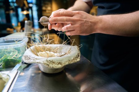 Foto de Chef macho cortado rociando especias con colador de té en ostra en plato de nido en la mesa en el restaurante. Concepto de deliciosa alimentación saludable - Imagen libre de derechos