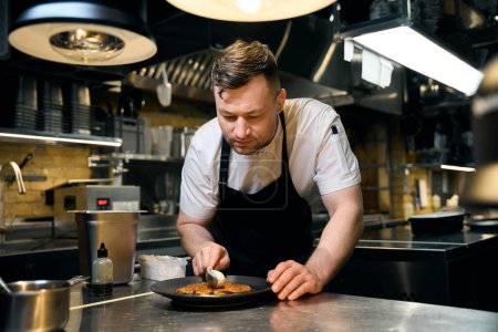 Téléchargez les photos : Chef masculin caucasien ajoutant de la crème dans une cuillère à frire gaufre sur une assiette à table au restaurant. Concept de délicieuse alimentation saine - en image libre de droit