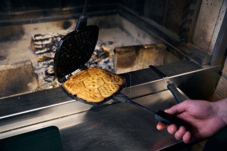 Selective focus of cropped male chef holding frying pancake in pancake maker in blurred fire place in restaurant. Concept of delicious healthy eating