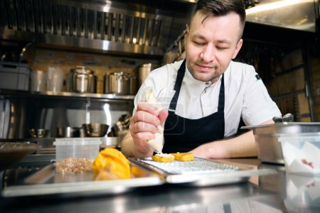 Téléchargez les photos : Chef européen étalant la crème sur un biscuit sur un plateau de fer net à table au restaurant. Concept de saine alimentation savoureuse - en image libre de droit