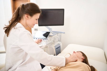 Téléchargez les photos : Médecin caucasien femme faisant une échographie de la glande thyroïde de la jeune femme sur le canapé médical à la clinique. Concept de soins de santé - en image libre de droit