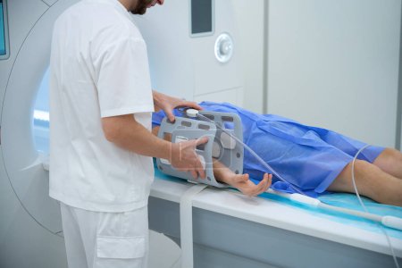 Photo recadrée du patient allongé sur une table d'IRM tandis que le professionnel de santé place une bobine d'extrémité autour de son avant-bras