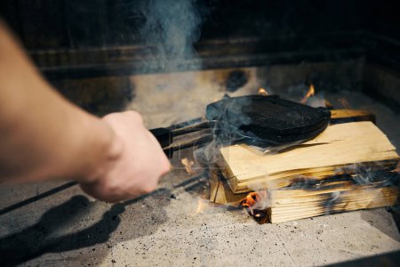 Person hand holding pancake maker over woods in burning open stove before food cooking in restaurant. Concept of tasty healthy eating