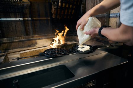 Cropped male chef pouring dough on pancake maker at burning fire place in restaurant. Concept of delicious healthy eating