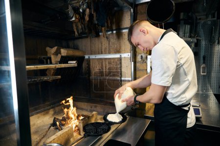 Side view of caucasian male chef pouring dough on pancake maker at burning fire place in restaurant. Concept of tasty healthy eating
