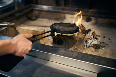 Cropped male chef hand frying pancake in pancake maker in burning fire place in restaurant. Concept of delicious healthy eating