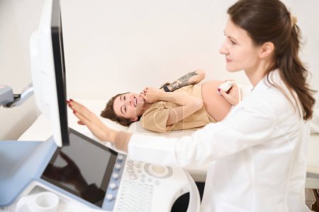 Foto de Ginecóloga caucásica haciendo ecografía de vientre embarazada de joven feliz mujer europea en clínica. Concepto de embarazo y maternidad - Imagen libre de derechos