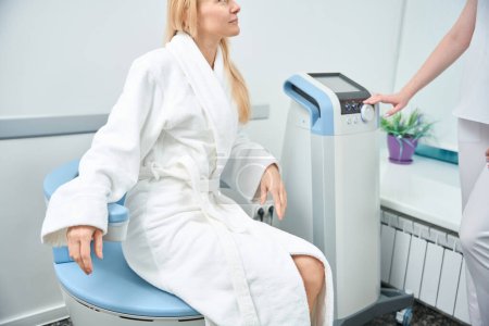 Krankenschwester, die Wellen elektromagnetischer Stimulation Stuhl während der Therapie der erwachsenen Frau, nicht-invasive und effektive Therapie, Stärkung der Muskeln