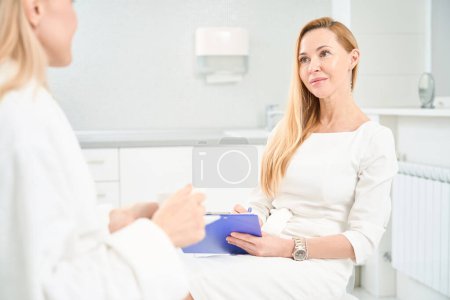Photo for Attractive general practitioner attentively listening to her female patient who came to rejuvenate and strength her skin and body, aesthetic medicine clinic - Royalty Free Image