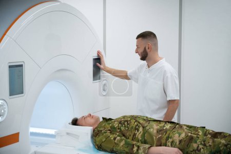 Technologe drückt Taste auf MRT-Scanner Portalsteuerung, während Servicemann auf dem Scan-Tisch liegt