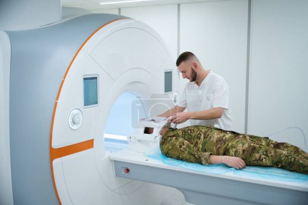 Militärpatient liegt auf MRT-Tisch, während sich Techniker Plastikspule um den Kopf legt