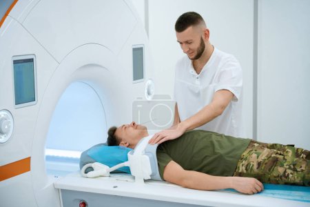 Radiographer placing coil over shoulder of military man positioned on magnetic resonance imaging table