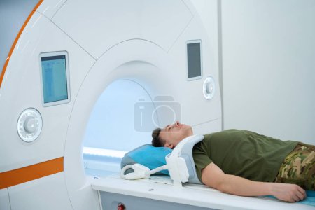 Serviceperson with coil placed over shoulder lying supine on magnetic resonance imaging table in scanning room