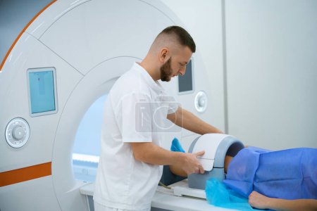 Mediziner legt Spule um Knie der männlichen Person auf Magnetresonanztomographie-Tisch