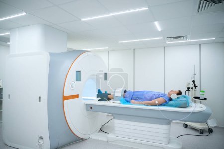 Patient mit Noise-Cancelling-Kopfhörern und Spule um das Knie liegend auf MRT-Tisch