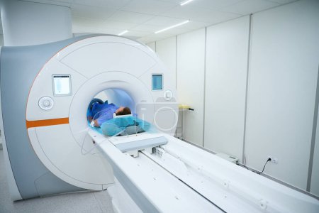 Patient in geräuschunterdrückenden Kopfhörern und Spule um das Knie gelegt, liegend auf dem Tisch im MRT-Portal