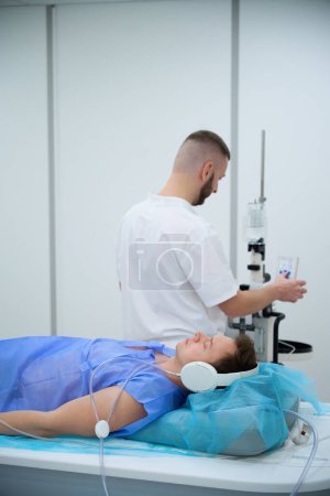 Patient in geräuschunterdrückenden Kopfhörern liegt auf Magnetresonanztomographie-Tisch, während Mediziner Taste am Kontrastinjektor drücken