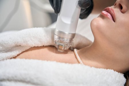 Close up of partial female beautician doing microneedle rf lifting of chest skin with IPL photorejuvenation device of young woman in blurred beauty salon. Concept of body skin care and rejuvenation