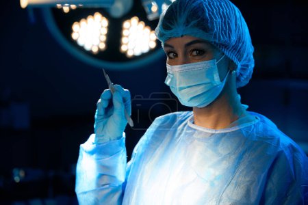 Doctor surgeon or nurse holding steel medical instrument on background of lamp in operating room