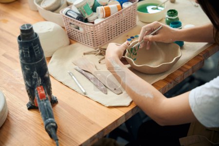 Femme méconnaissable décoration bol de vaisselle dans l'atelier de céramique de poterie d'argile