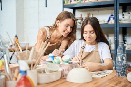 Femme potier peinture bol en céramique fait à la main avec son professeur en atelier de poterie