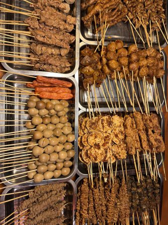 Téléchargez les photos : Angkringan est une poussette en bois pour vendre divers types de nourriture et de boissons traditionnelles sur le bord de la route en Indonésie. Différents types de menu satay prêt à être brûlé. - en image libre de droit