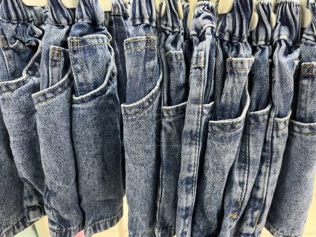 Téléchargez les photos : Neat rows of jeans on hangers. the jeans are ready to be displayed to the customer. Various forms of jeans are soft and smooth. Trouser hanger for display. Bright colored fabric background concept. - en image libre de droit
