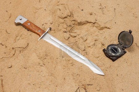 Téléchargez les photos : Baïonnette de couteau avec poignée en bois coincée pour fusil automatique dans le sable - en image libre de droit