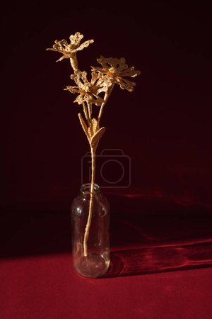 A glass vase with a bouquet of flowers made from straw on the red background. The flower is illuminated by the sun. Small depth of field. 