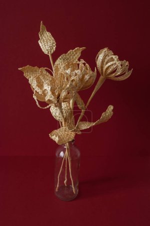 A glass vase with a bouquet of flowers made from straw on the red background. Straw weaving