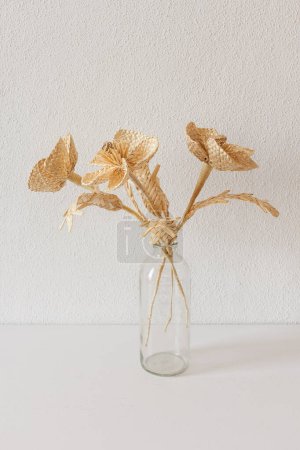 A glass vase with a bouquet of flowers made from straw on a white background. Straw weaving