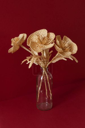 A glass vase with a bouquet of flowers made from straw on the red background. Straw weaving