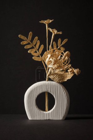 Eine hölzerne Vase mit einem Blumenstrauß aus Stroh auf schwarzem Hintergrund. Strohflechten